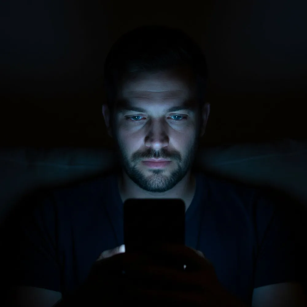 Homem olhando para o celular em um ambiente escuro